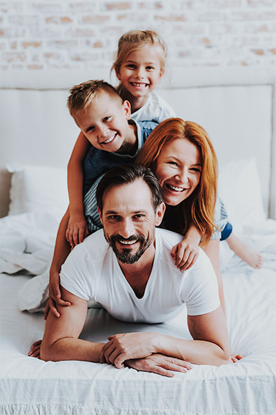 Smiling Man And Woman Laying On Bed With Kids